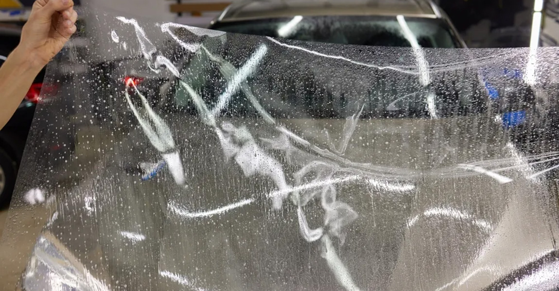 transparent protective film being applied to car hood by professional PPF installer