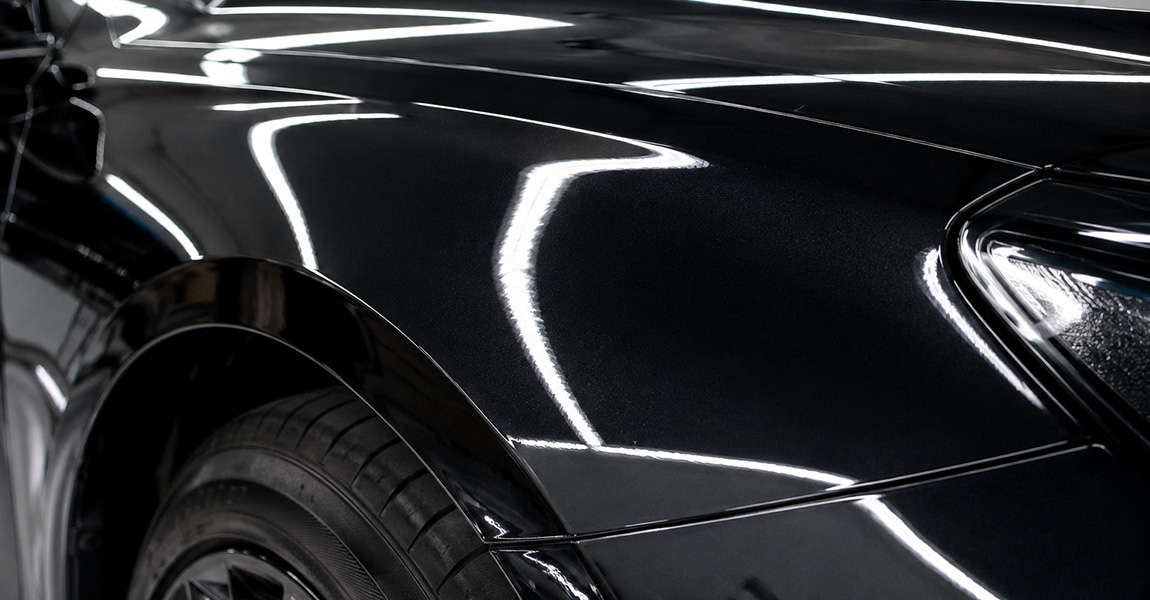 Reflective close-up of clear paint protection film showing high gloss and clarity on a dark car panel